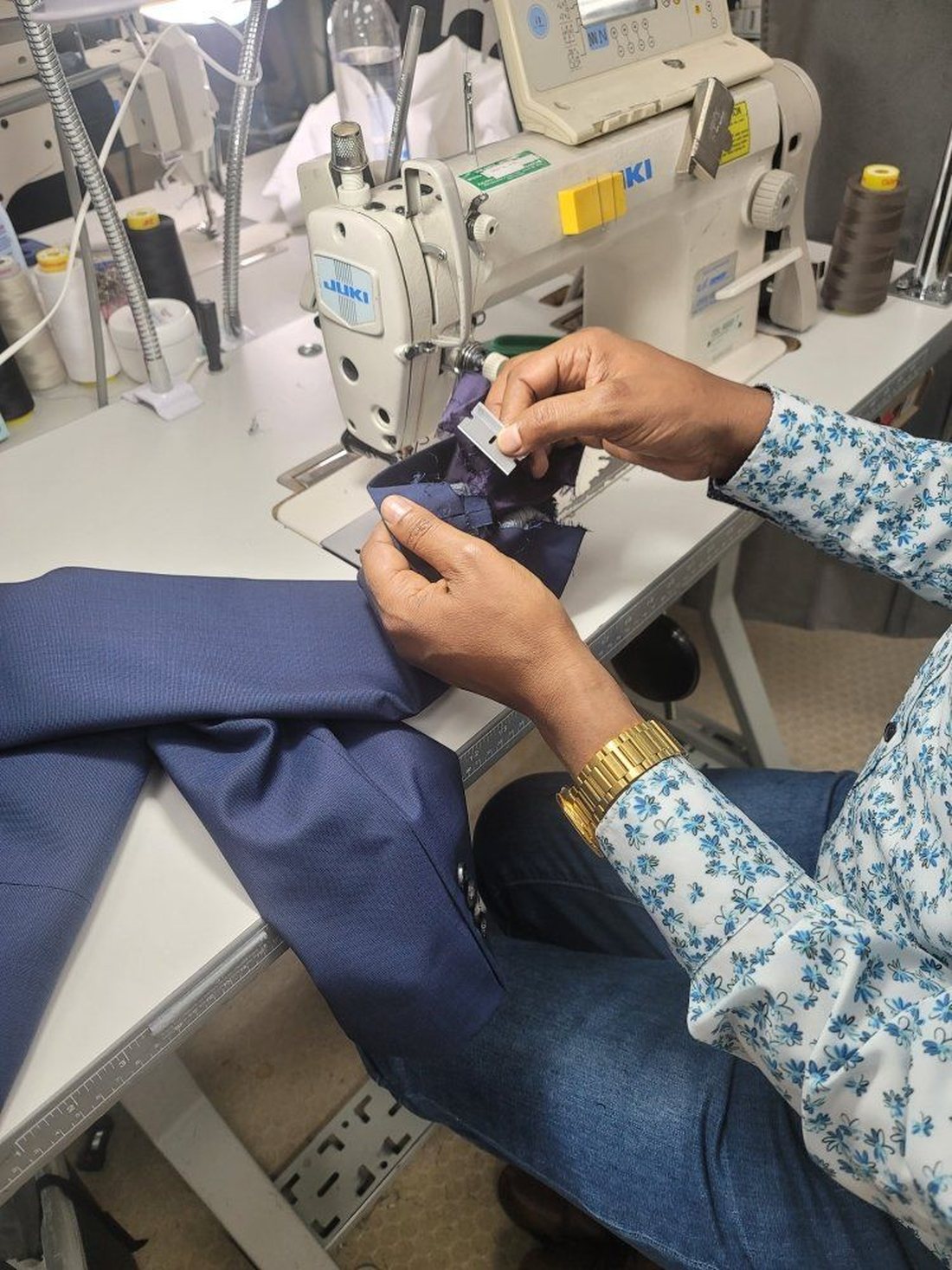 Ali trimming a seam on a navy suit jacket at the sewing machine in the Denver shop